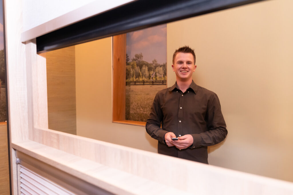 Jochem de vierde generatie, bedient elektrische raambekleding lachend in de showroom van Woninginrichting van der Velden