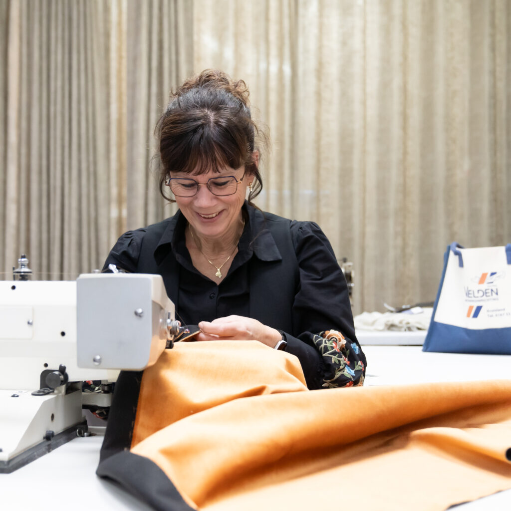 Ingrid achter de naaimachine terwijl ze een gordijn op maat afwerkt in het atelier.